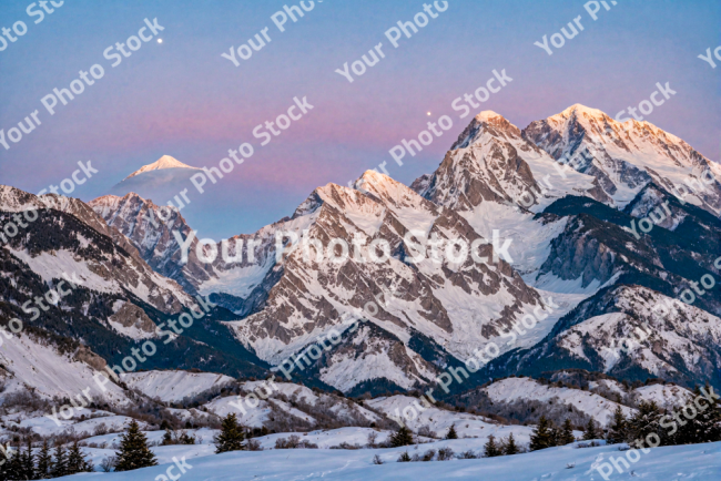 Stock Photo of Snowy mountains at sunset with pine trees on the slope