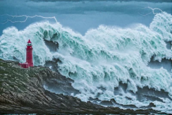 Stock Photo of Red lighthouse in the rock hit by sea storm